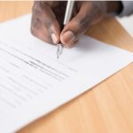 a male hand holding a fountain pen and signing a document