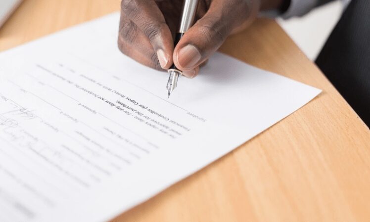 a male hand holding a fountain pen and signing a document